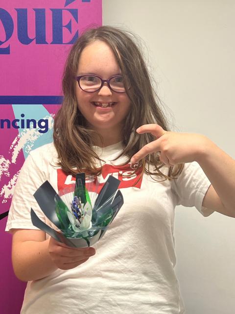 Image of a young person smiling while holding a handmake flower made from recycled plastic 