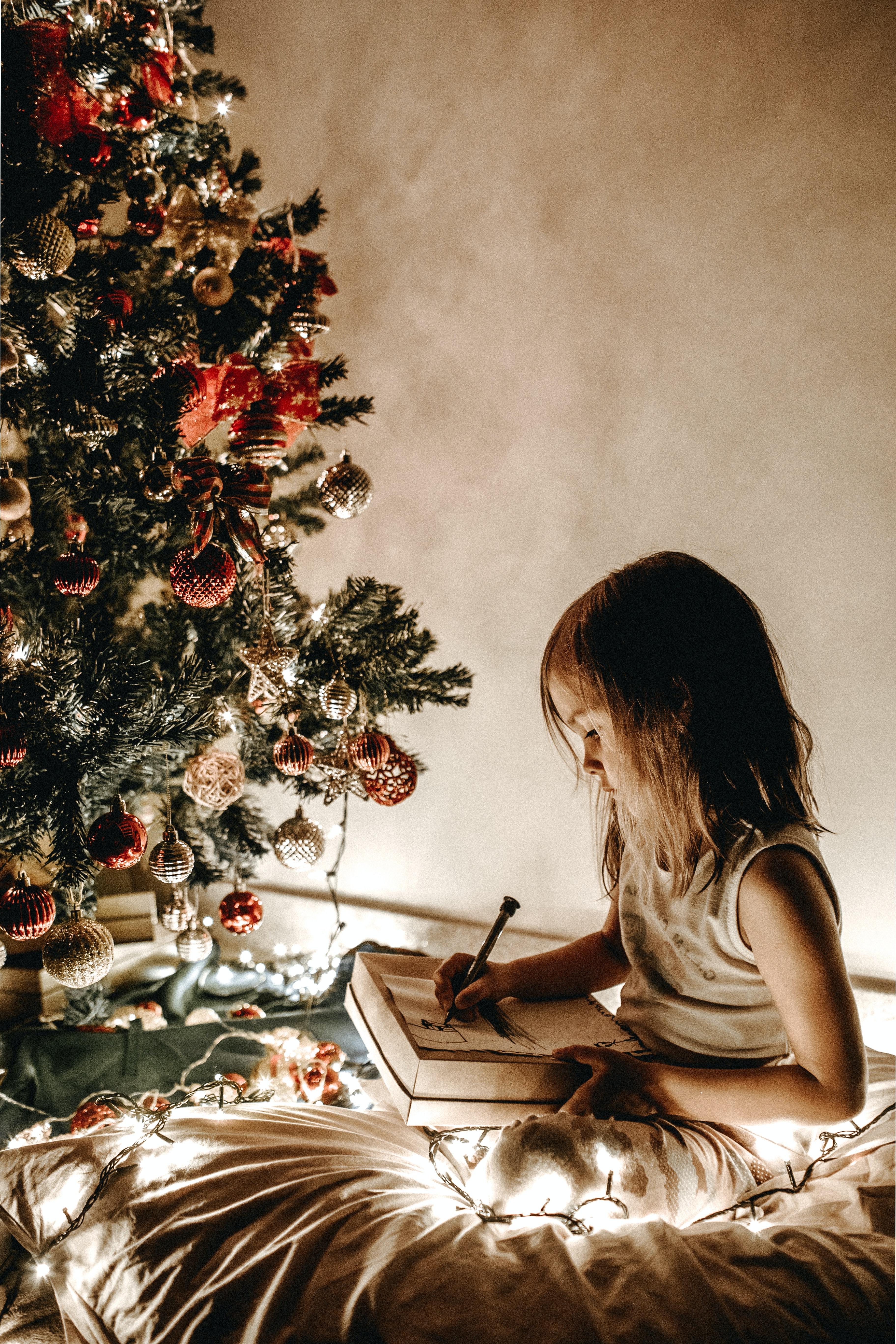 Child sitting next to Christmas tree