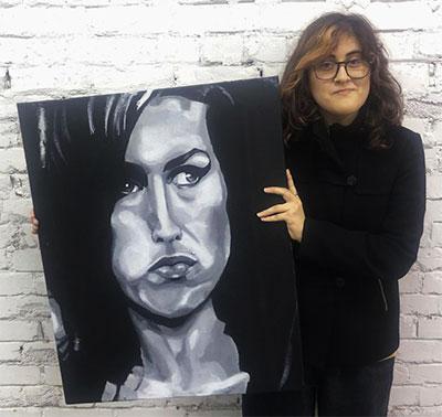 Image of young person holding their hand painted portrait of Amy Winehouse