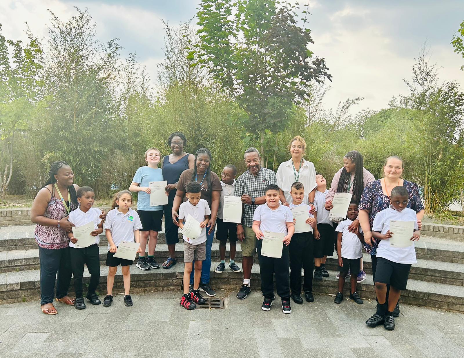 The picture is of children and staff at The Brook Special School in Broadwater Farm, with the children proudly holding up their AQA accreditation certificates.