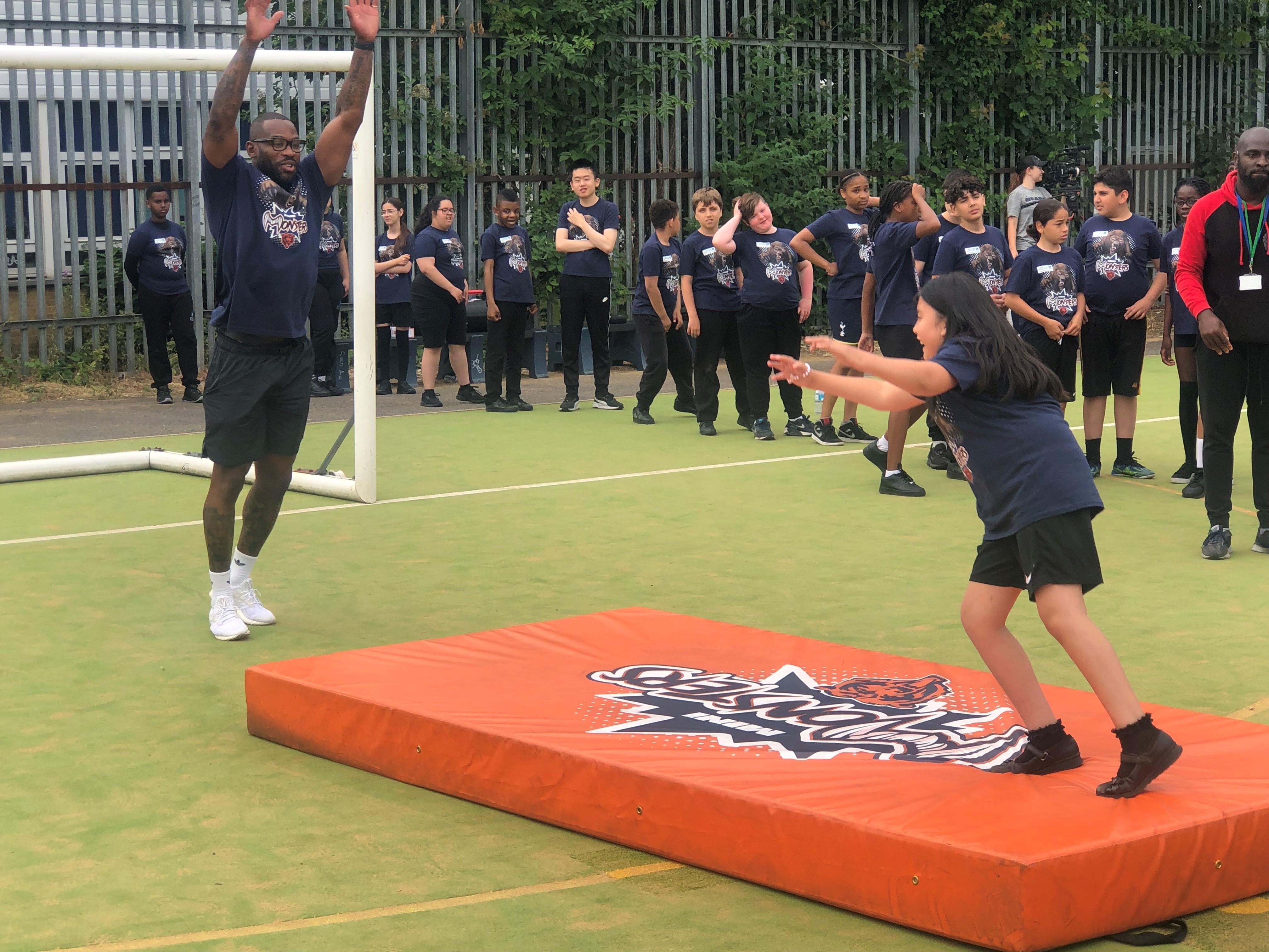 The pic is of former Harlequins, England & British & Irish Lions rugby player Ugo Monye reaching up in the air with his arms outstretched as a young pupil attempts to catch a pass during the 'Mini Monsters' camp at Duke's Aldridge Academy.